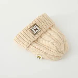 Gros plan sur la maille torsadée et l'étiquette en cuir brun d'un bonnet d'hiver beige