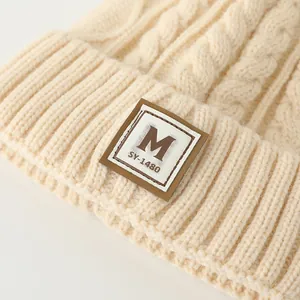 Gros plan détaillé du bonnet en maille beige avec étiquette lettre M et bordure côtelée