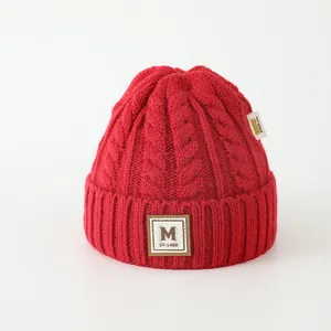 Détail du bonnet rouge foncé en maille torsadée avec écusson lettre M et texture épaisse