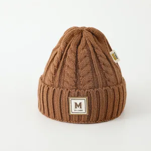 Détail d'un bonnet en maille torsadée marron avec écusson M et bord côtelé