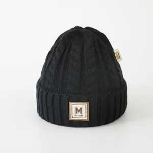 Détail d'un bonnet d'hiver en grosse maille avec écusson en cuir M et texture torsadée