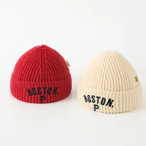 Detail of red and beige knitted beanies showing thick texture and Boston P embroidery