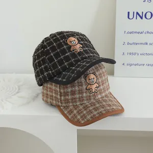 Détail de casquettes en laine à carreaux avec broderie d'ours aux couleurs d'automne