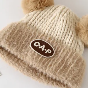 Detail of baby knit hat with CAP patch and fluffy faux fur double pom-poms