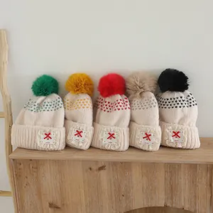 Close-up of five knitted beanies with fluffy pom-poms and lace patches on a wooden shelf