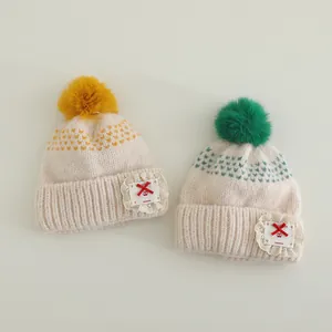 Detailed view of handmade knitted children's hat with lace patch and soft fur pom-pom