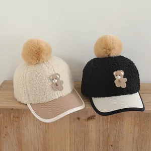 Detail of winter baseball caps for kids with teddy patch and fluffy pom-pom on wooden bench