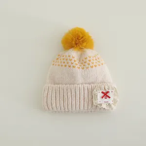 Detail of baby knit hat showing yellow heart patterns and handmade lace patch