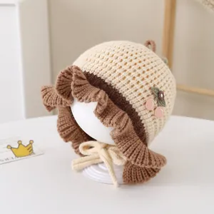 Dettaglio del bordo in pizzo e decoro ciliegia sulla cuffia in maglia beige neonato