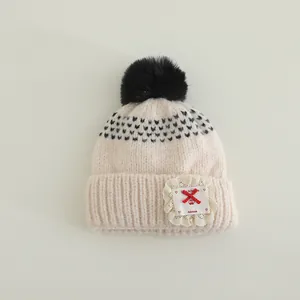 Detailed view of knitted winter hat featuring a fluffy pom pom and lace patch detail