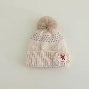 Detail of knit baby beanie with large faux fur pom-pom and lace cherry patch