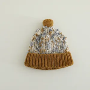 Detailaufnahme der Wintermütze mit Schneeflockengarn Textur und braunem Bommel