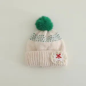 Detail of knit beanie showing lace applique with handmade embroidery and faux fur pompom