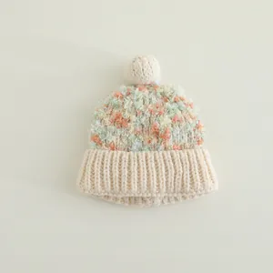 Nahaufnahme der bunten Strickstruktur und des weißen Bommels dieser Kinder-Wintermütze