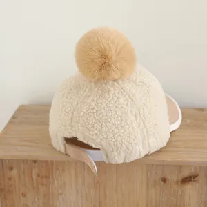 Détail de la casquette en peluche crème avec grand pompon en fausse fourrure et sangle