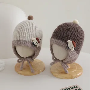 Detail of baby knit earflap hat with plush pompom and cute bear patch in warm brown tones