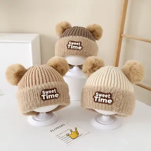 Detailed knit texture of cozy baby beanies with fluffy pom poms and leather patch