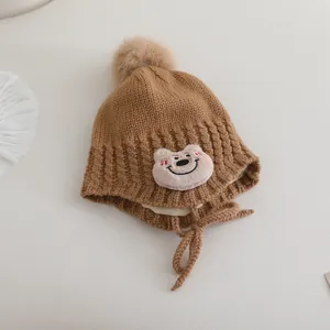 Dettaglio di un berretto in maglia marrone per bambini con patch orsetto rosa e pompon