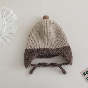 Close-up of dual-tone knit baby hat with ear flaps and a plush pompom on top