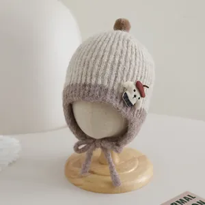 Detail of knit baby hat with earflaps, pom-pom and bear patch in beige and brown