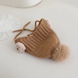Dettaglio ravvicinato del cappello in maglia marrone con paraorecchie e pompon soffice