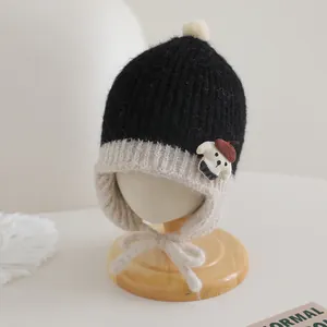 Close-up of knit baby earflap hat with pom-pom and bear patch detail