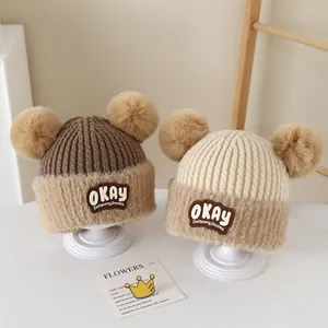Detail of warm baby knit hats with pom-poms, faux fur lining, and OKAY patch embroidery