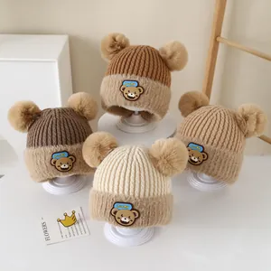 Detailed view of knitted baby hats with plush double pom-poms and cute bear patch