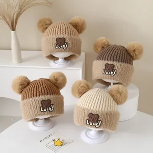Detail view of double pom-pom knit baby hats with cute bear patches in earthy tones