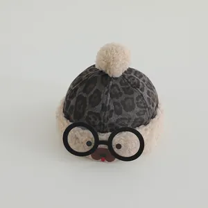Close-up of leopard print baby winter hat with fur pompom and cartoon bear face details
