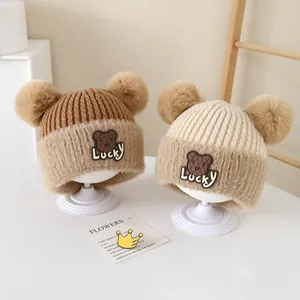 Detail of warm knit baby hats with pom-poms and cute lucky bear embroidery patch