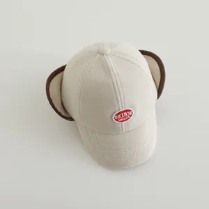 Close-up of beige fleece toddler baseball hat with earflaps and embroidered patch