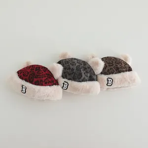 Close-up of baby winter leopard print hats with plush pom-poms and embroidered letter B