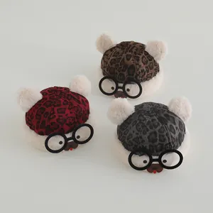 Detailed view of three leopard print baby hats with plush ears and round glasses decor