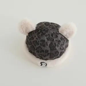 Close-up of baby leopard print winter hat with double pom-poms and white faux fur trim