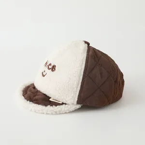 Detailed view of the 'Nice' smiley embroidery and brown quilted fabric on baby cap