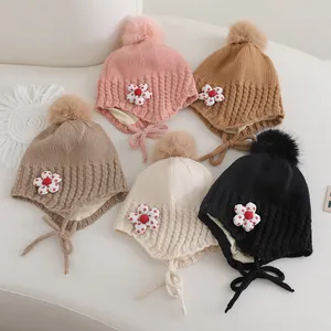 Détail de bonnets tricotés pour bébé avec pompons et patchs floraux en cinq couleurs