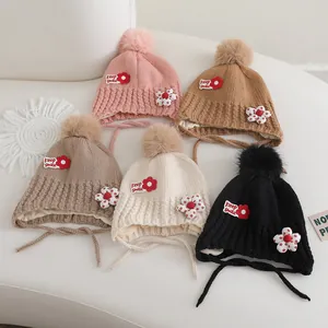 Détail de bonnets en tricot avec cache-oreilles, pompons et broderies florales multicolores