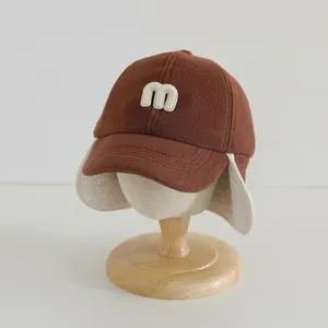 Brown winter baseball cap with earflaps and m embroidery on a wooden stand