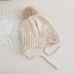 Détail d'un bonnet en tricot crème pour bébé avec pompon marron et lanières tressées