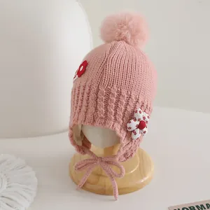 Détail du bonnet tricoté rose pour bébé avec pompons et applique florale délicate