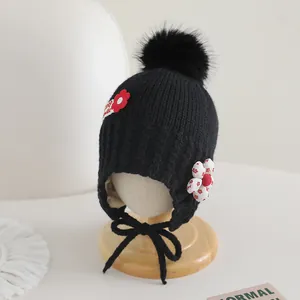 Détail du bonnet en tricot noir pour bébé avec pompon en fourrure et broderie florale