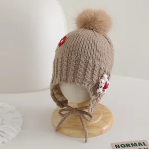 Détail du bonnet en tricot pour bébé avec pompon et écusson floral sur tissu côtelé kaki