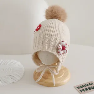 Détail du bonnet en tricot pour enfants avec cache-oreilles, fleurs et pompon marron