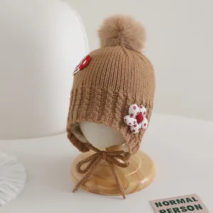 Détail d'un bonnet tricoté marron pour bébé avec pompon et fleurs en relief