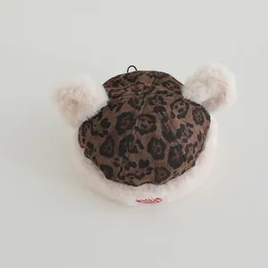 Detail of leopard print plush baby hat with two soft beige pom-poms and front label