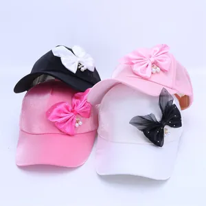 Detalle de gorras infantiles con lazos de lentejuelas, paneles de malla y dijes de perlas
