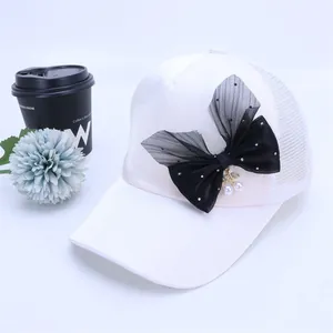 Detalle de gorra blanca de rejilla con lazo negro y colgantes de perlas blancas