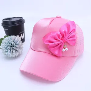 Detalle de gorra rosa para niña con lazo de satén, pedrería y cerezas de perlas