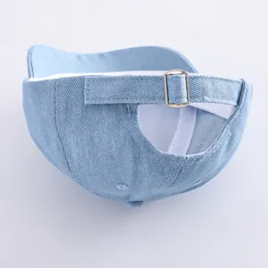 Detail view of adjustable metal buckle and stitching on light blue denim baby cap